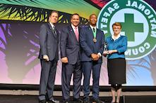 image of four men and one woman in professional attire standing on a stage with a sign in the background reading National Safety Council